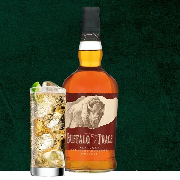 Buffalo Trace Bourbonflasche neben Longdrinkglas mit Ginger Ale, Eis und Limette vor dunkelgrünem Hintergrund
